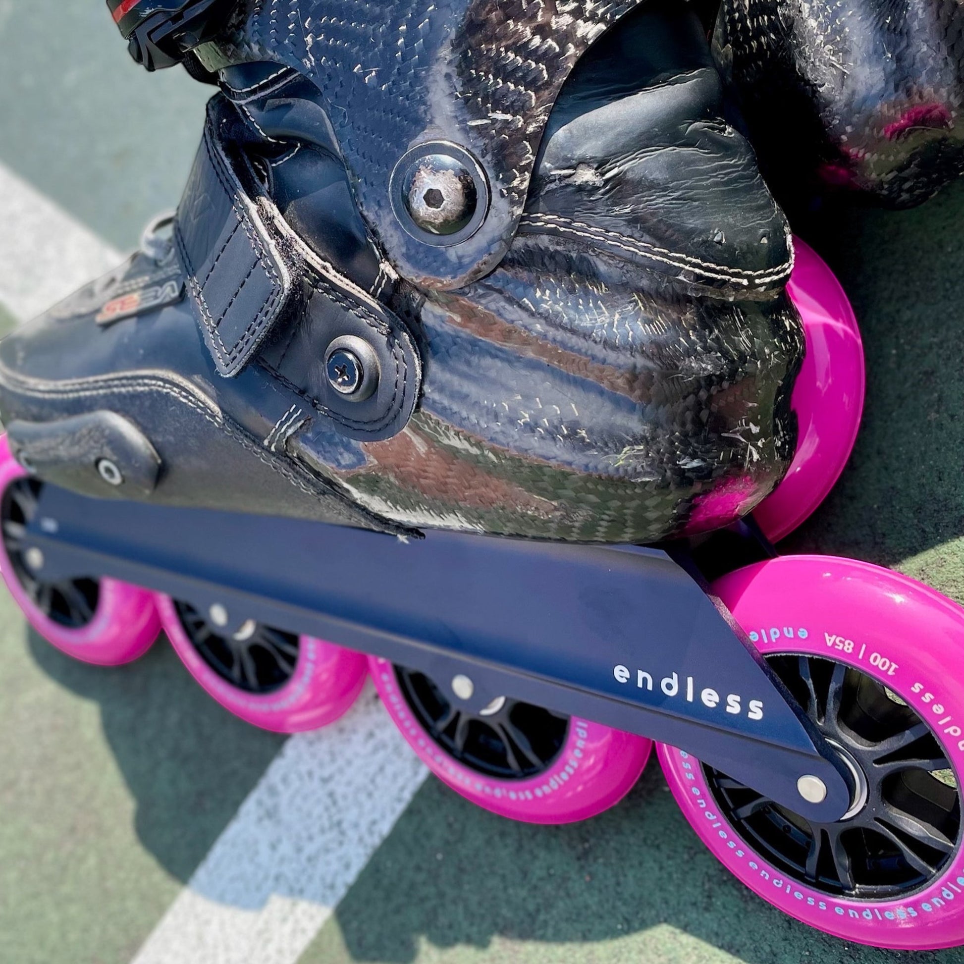 Endless Blading Co. navy UFS frame with four bright pink 100mm wheels on a black skate boot.