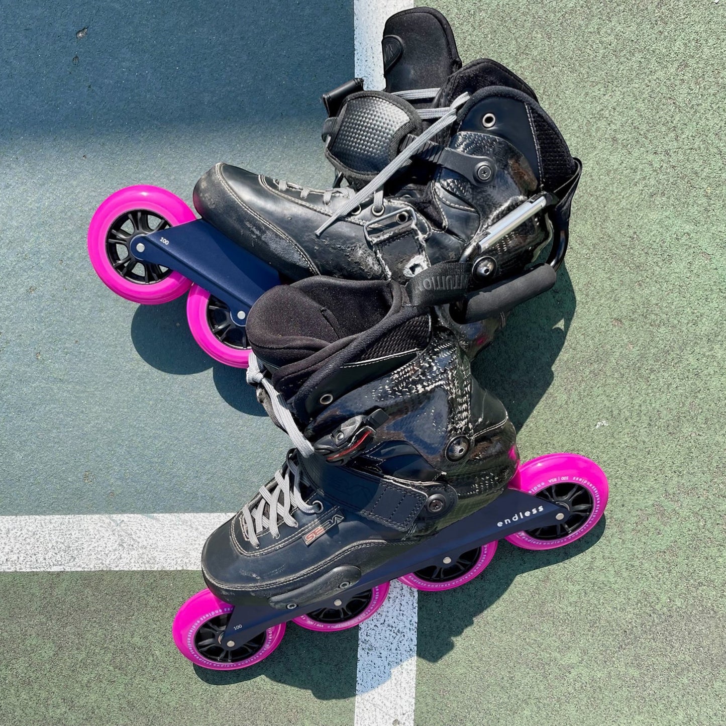 Endless Blading Co. black UFS inline skate frames with four 100mm bright pink wheels.