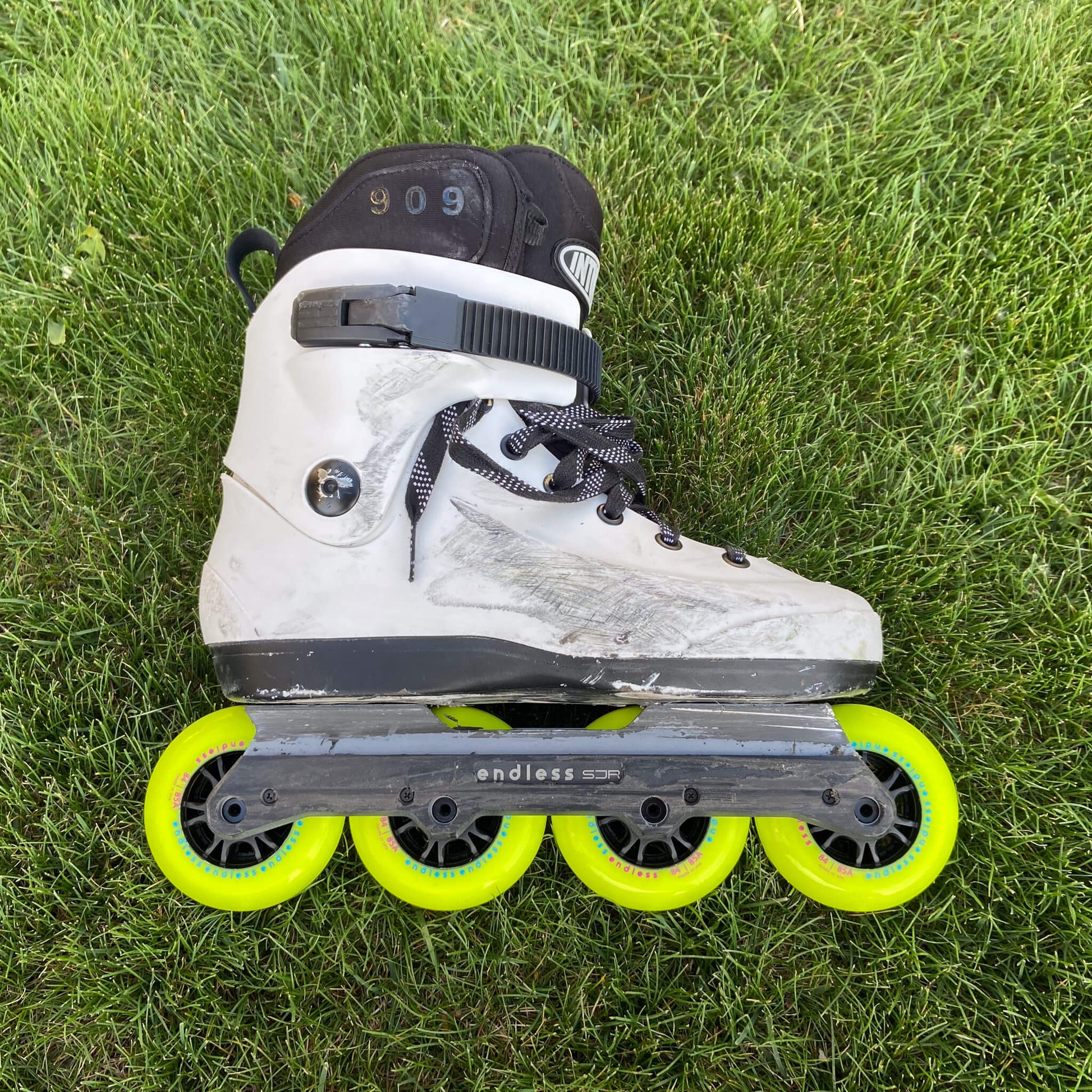 Endless Blading Co. SJR UFS frame with slider in gray mounted on a white aggressive skate with bright neon green wheels on grass