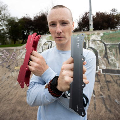 Endless Blading Co. SJR UFS frames in light red and grey held by Stephen Johnstone at a skate park.
