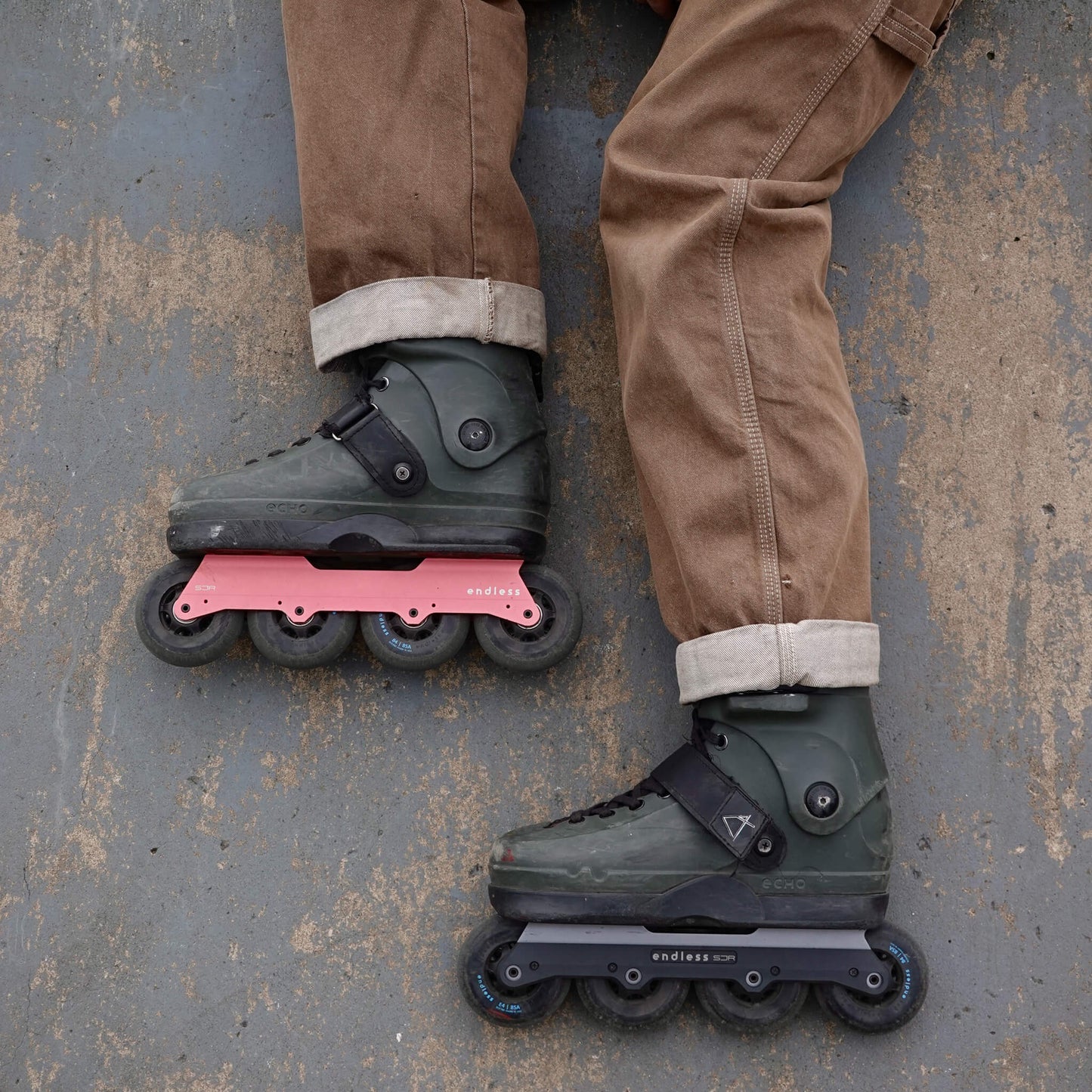 Endless Blading Co. SJR UFS frames in pink and black mounted on olive green aggressive skates on concrete ground